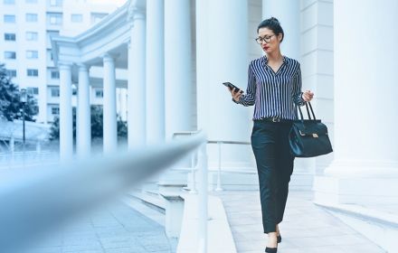Woman walking near building while using smart phone