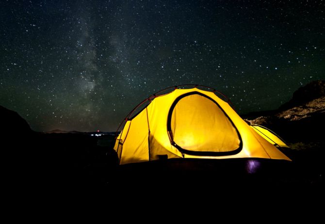 Yellow camping and hiking tent at night under shining stars