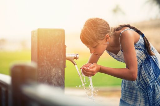 Young girl drinking water from tap with her hands