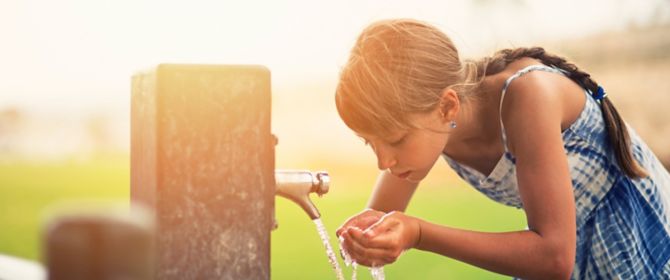 Young girl drinking water from tap with her hands